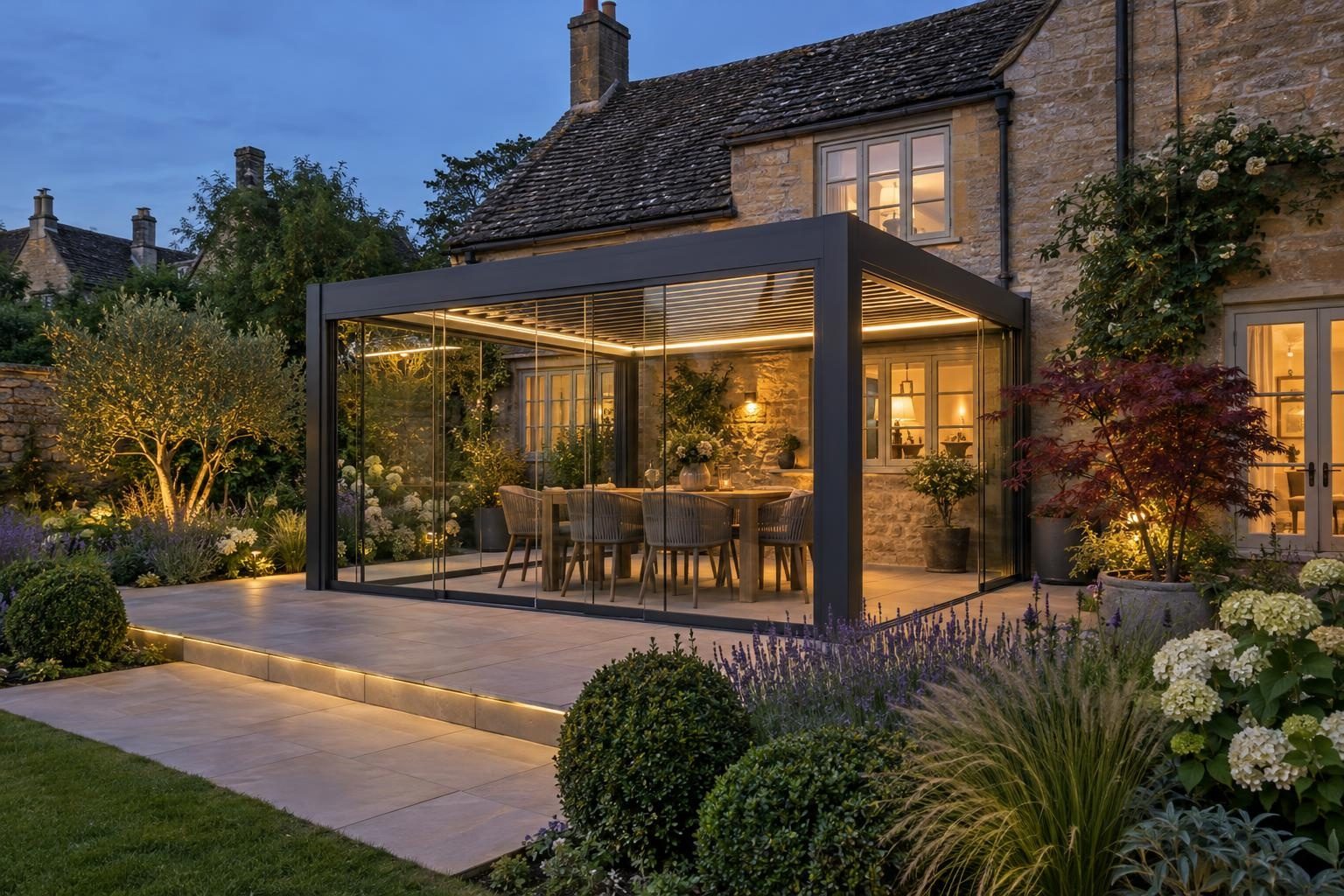 Anthracite louvred pergola closed in with glass sliding doors beside a stone cottage at dusk Anthracite louvred pergola closed in with glass sliding doors beside a stone cottage at dusk