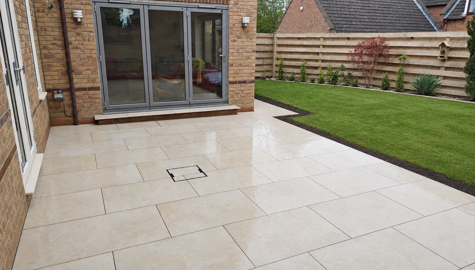Light large-format porcelain patio outside grey bifold doors with a lawn beyond in Stamford